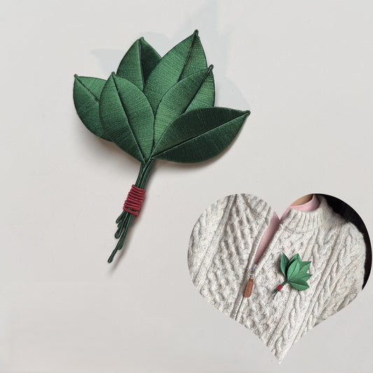 Handmade silk wrapped flower brooch pin in green leaf design, worn on a white cable knit sweater.