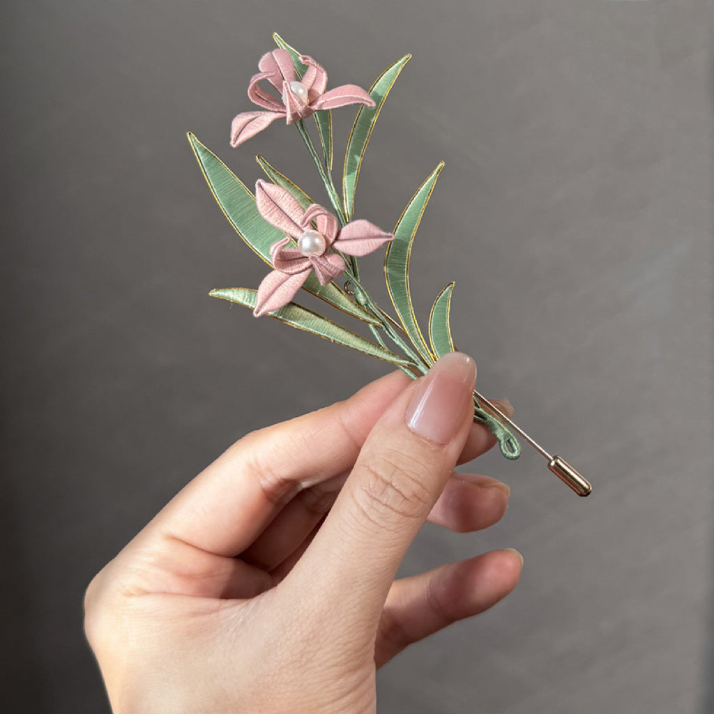 DIY Kit for Orchid Chanhua Brooch featuring pink silk-wrapped petals, green leaves with gold wire edges, and a pearl center on a brooch pin.