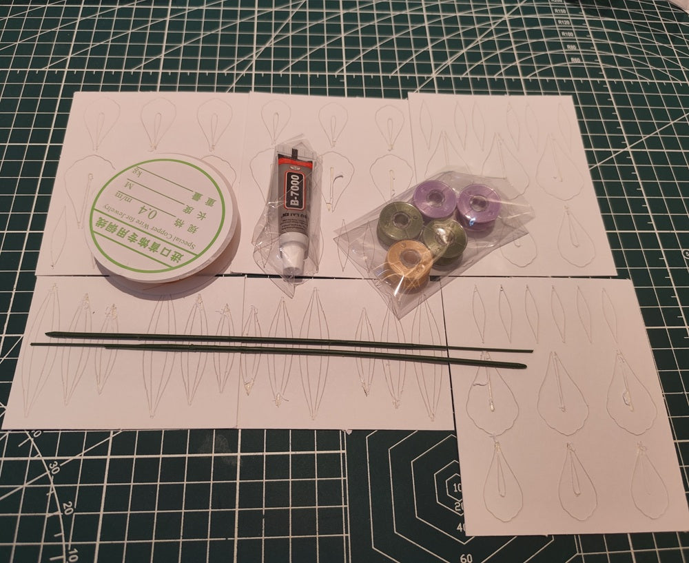 The materials for the Iris Chanhua DIY flower kit, including spools of thread, copper wire, paper templates, and floral stems, laid out on a craft mat.