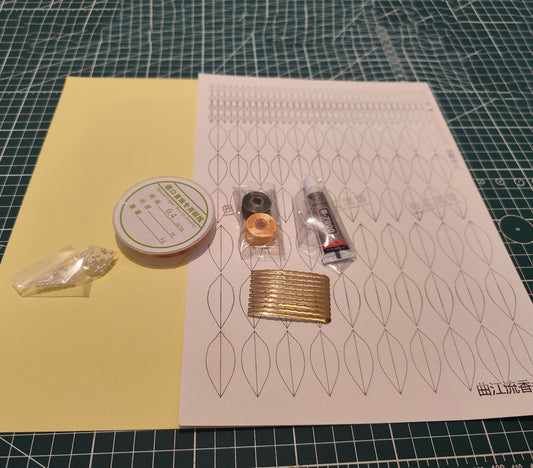 The contents of the Golden Osmanthus DIY flower kit, including spools of thread, copper wire, pearls, glue, a comb base, and paper templates on a craft mat.