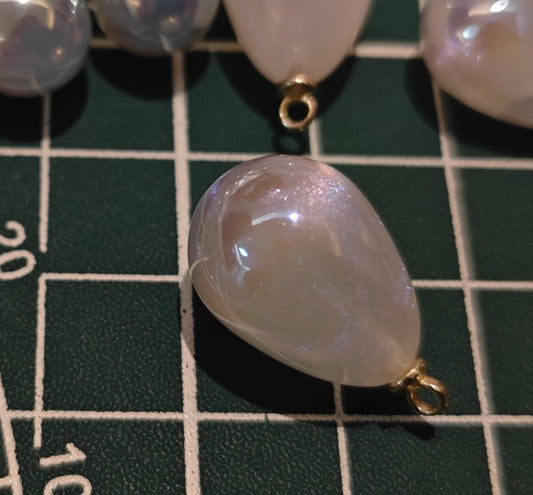Macro shot of a single white pearlescent charm showing fine internal glitter and teardrop shape for DIY supplies.