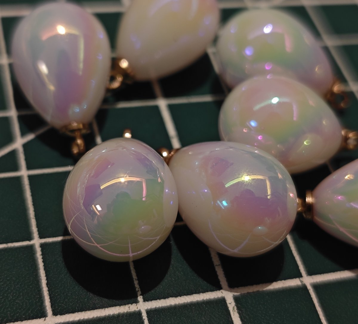 Macro shot of two iridescent tear drop charms, highlighting the opal-like sheen and subtle sparkle for DIY earring making.
