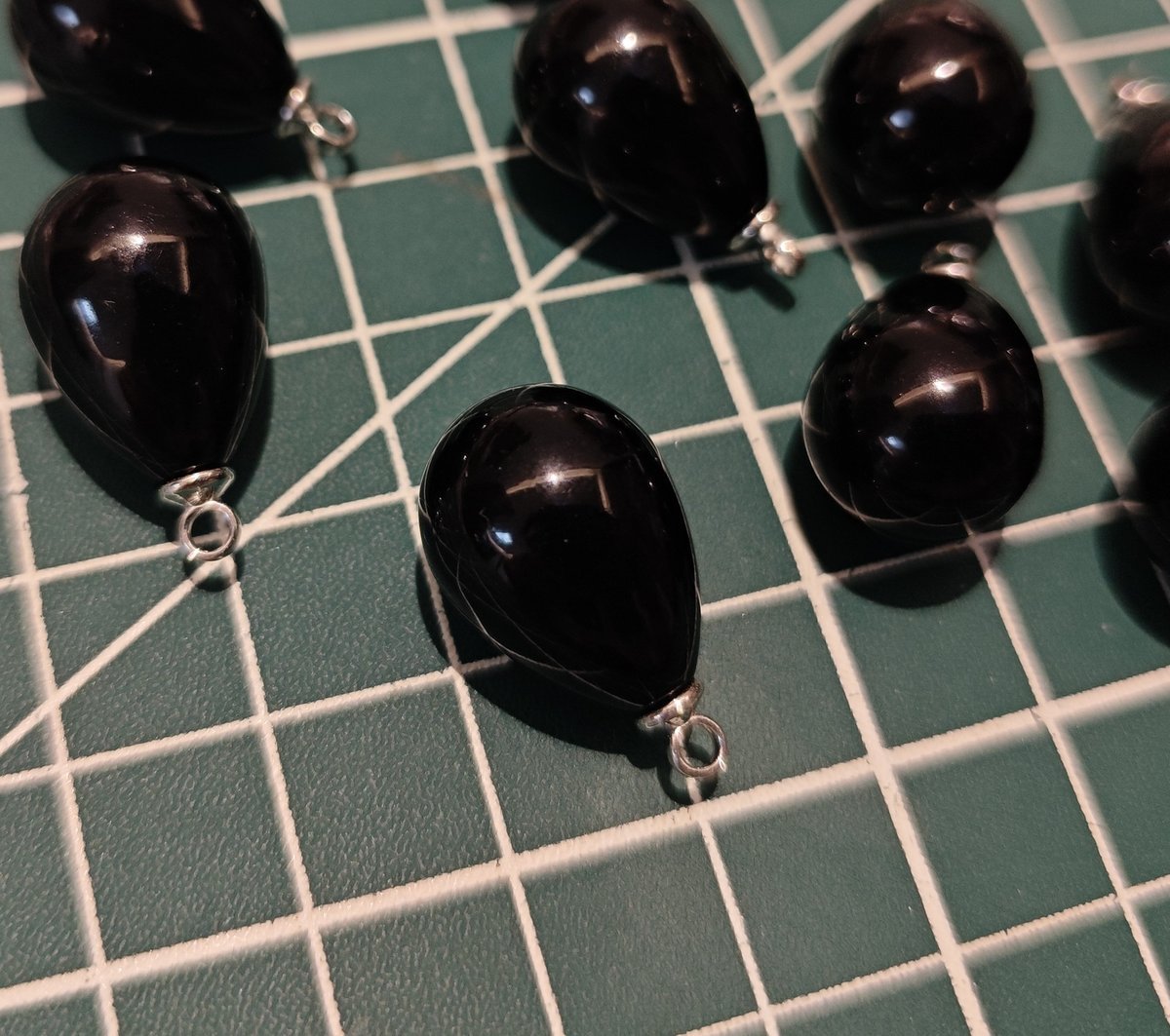 Close-up of several black tear drop charms, showing high shine and reflective finish for earring making.