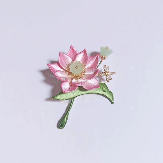 Chanhua handmade pink lotus brooch with jade-green center, gold stamens, green leaf stem, jade seed pod bud, and crystal dragonfly accent, displayed on a light gray background
