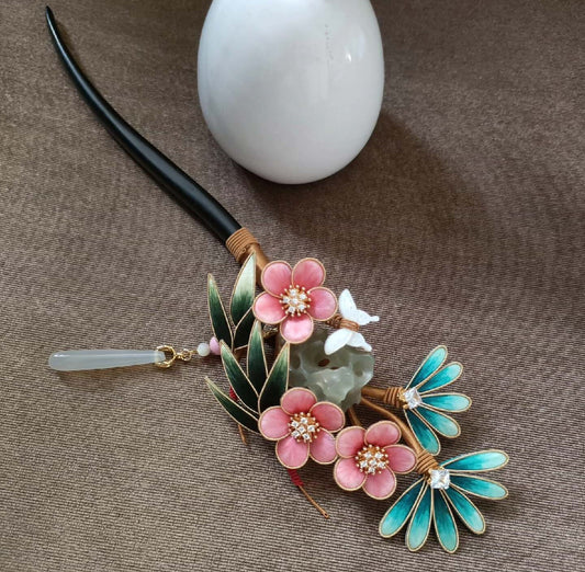Ronghua handmade pine bamboo plum hairpin with three pink plum blossoms, dark green pine leaves, teal bamboo accents, white butterfly, carved rock, jade drop pendant, and dark wooden pin, displayed on grey fabric