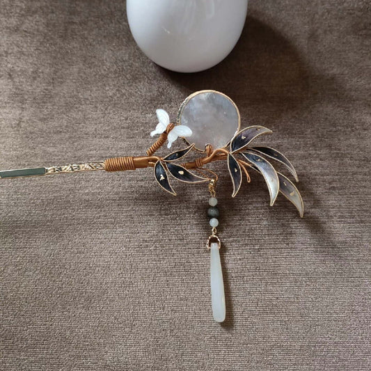 Ronghua handmade bamboo and moon hairpin with dark grey-brown velvet leaves, translucent round moon disc in copper wire, crystal butterfly, and jade drop pendant on a gold twisted pin, held against a light grey background