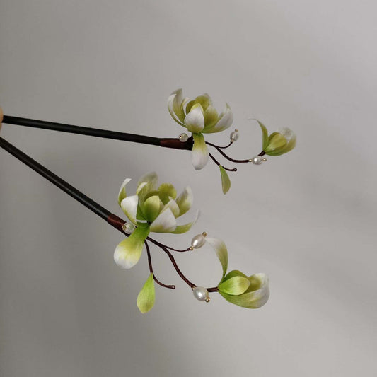 Ronghua handmade magnolia hairpin with white and green silk petals, two green buds, dark brown wire branches, pearl accents, and a dark wooden pin, displayed against a light gray background