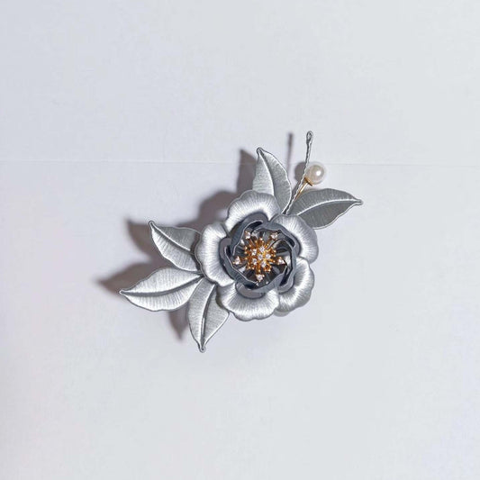 Chanhua handmade ink camellia brooch with silver-grey layered petals, gold crystal stamen center, grey leaves, and pearl sprig, displayed on a white background