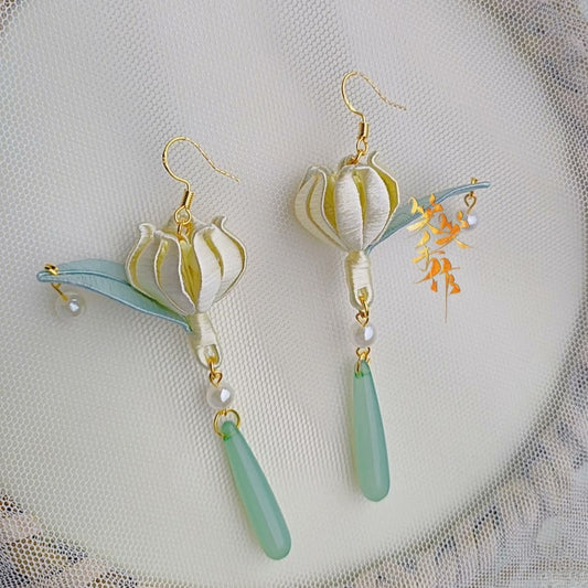 Close-up of the handcrafted Chanhua bloom earrings, showcasing intricate folded fabric petals, with 925 silver hooks and dangling freshwater pearls and green teardrop beads.