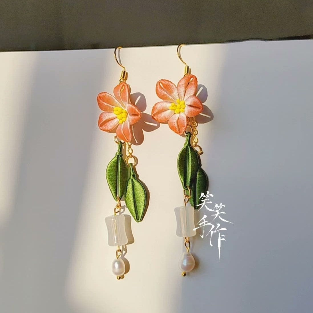 Artisan-made Chanhua earrings featuring orange silk flowers, green fabric leaves, and dangling freshwater pearls, designed for both daily wear and special occasions.