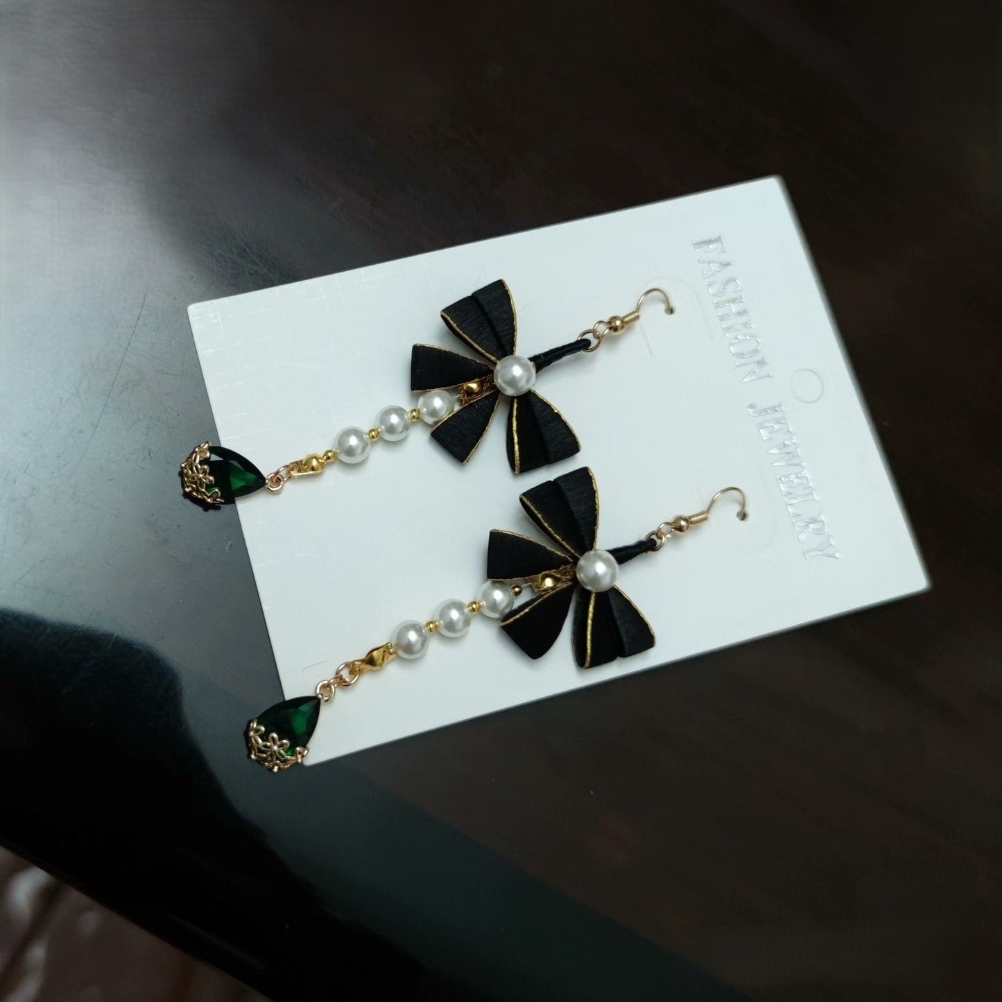 Close-up of elegant black Chanhua ribbon earrings with pearls and a green drop gem.