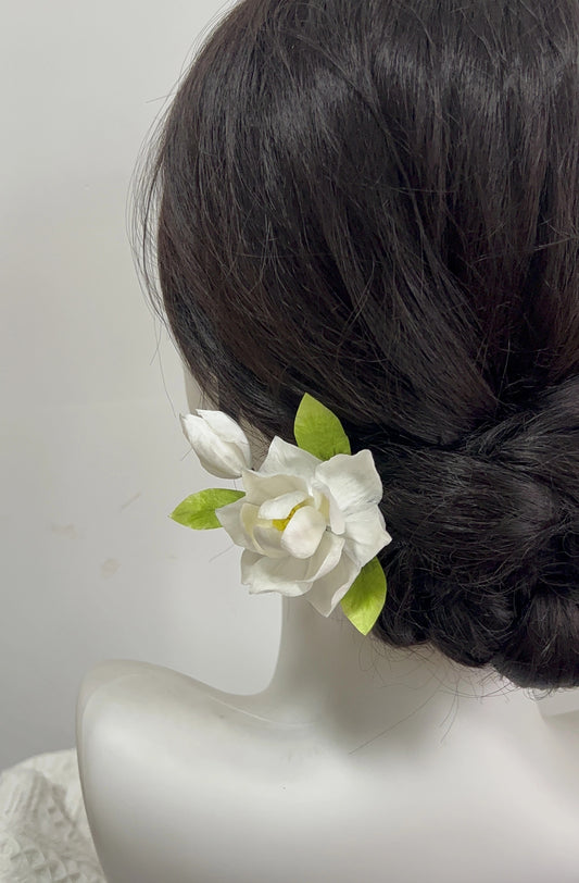 Handmade white mulberry silk Ronghua Gardenia flower hair pin with green leaves and bud, styled near the ear in a dark updo.