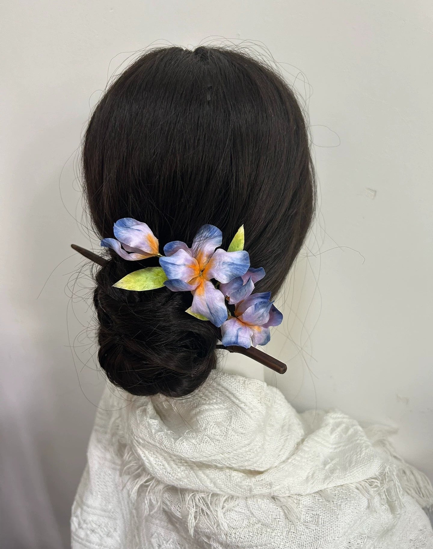 Handmade blue-purple iris flower hair stick made from natural silk thread on mannequin bun hairstyle.