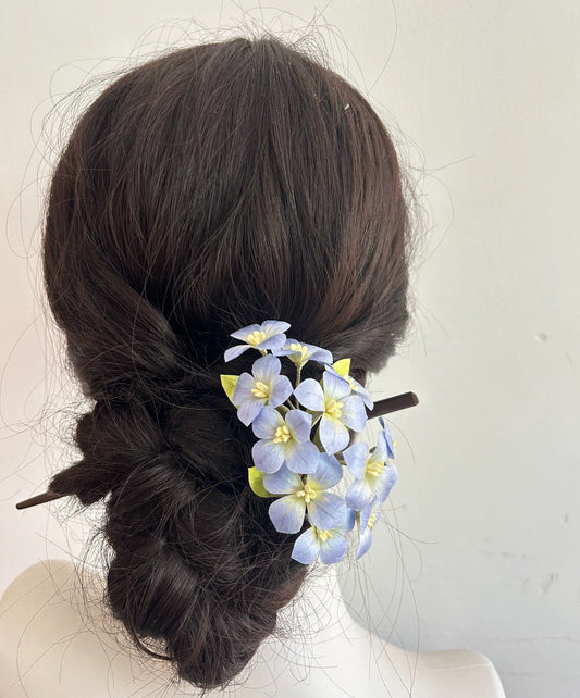Rear view of blue silk hydrangea flower hair stick in bun hairstyle on mannequin.