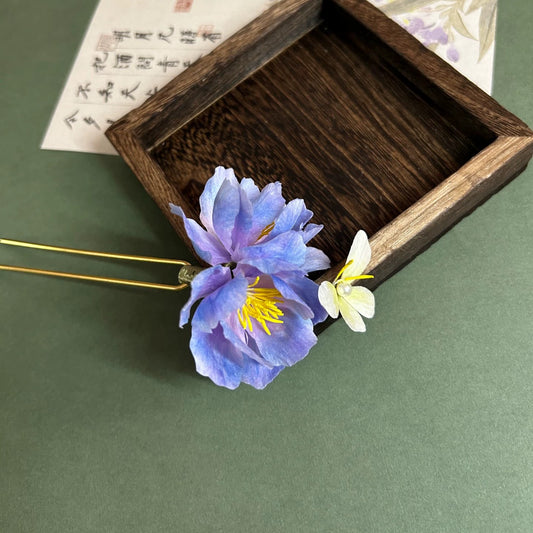 Close-up of gradient blue-purple velvet Ronghua cotton rose hair stick with tiny white flower and pearl detail on wooden tray