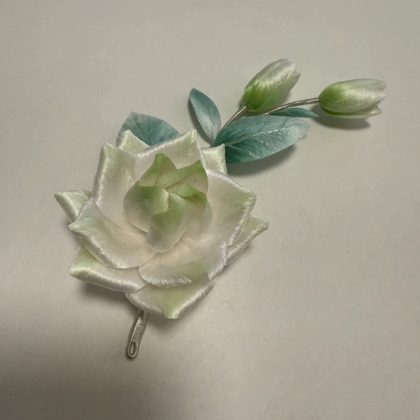 Handmade Ronghua gardenia flower brooch in ivory and pale green mulberry silk with mint leaves, close-up view