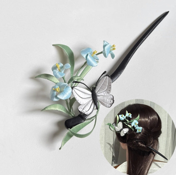 A finished handmade Chanhua hairpin featuring light-blue silk flowers, green leaves, and a white butterfly. An inset image shows the hairpin elegantly worn in a woman's hair.
