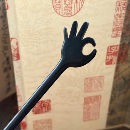 Natural African Blackwood hair stick with OK gesture design 18cm on traditional scroll background.
