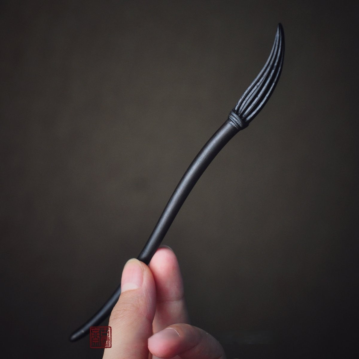 Natural African Blackwood hair stick with calligraphy brush design 19.8cm held in hand against dark background.