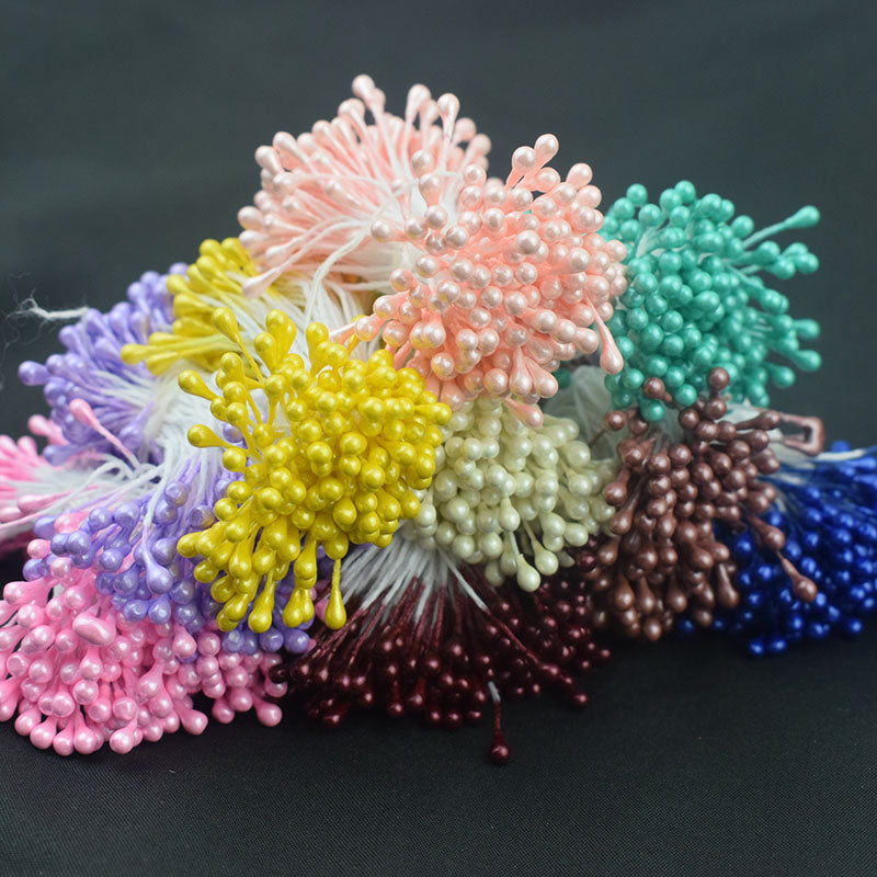 A vibrant assortment of 3mm glossy artificial flower stamens in various colors, including pink, yellow, blue, and brown, arranged on a dark background.