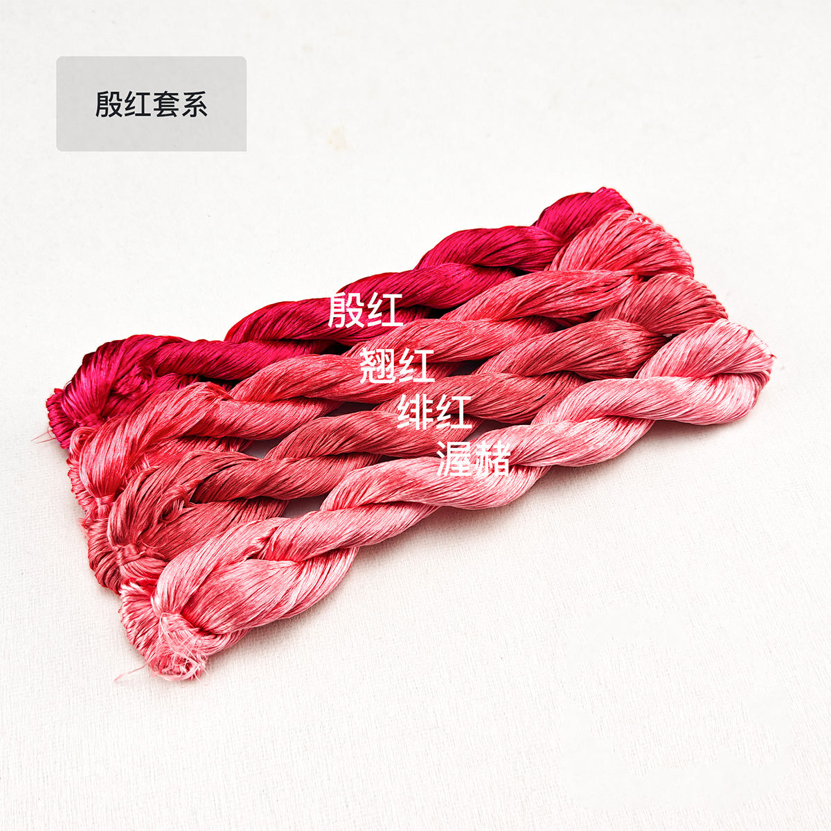 Hand-dyed Suzhou thick mulberry silk thread in the Yin Hong Red series, showing a gradient of five lustrous red and pink skeins for making Ronghua (velvet flowers).