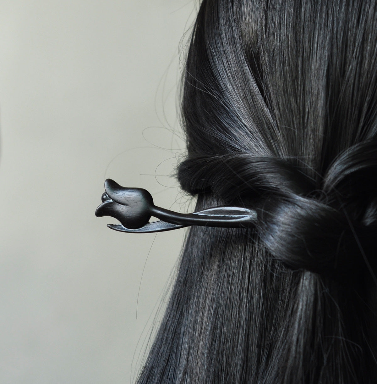 A dark ebony wood tulip hair stick shown securing a twisted hairstyle in long, black, shiny hair.