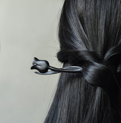 A dark ebony wood tulip hair stick shown securing a twisted hairstyle in long, black, shiny hair.