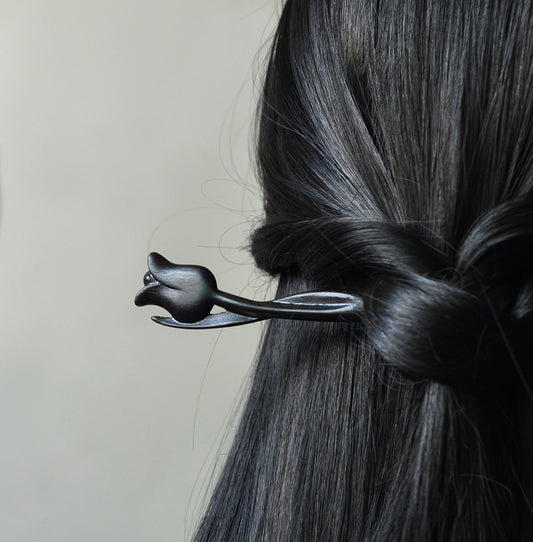 A dark ebony wood tulip hair stick shown securing a twisted hairstyle in long, black, shiny hair.