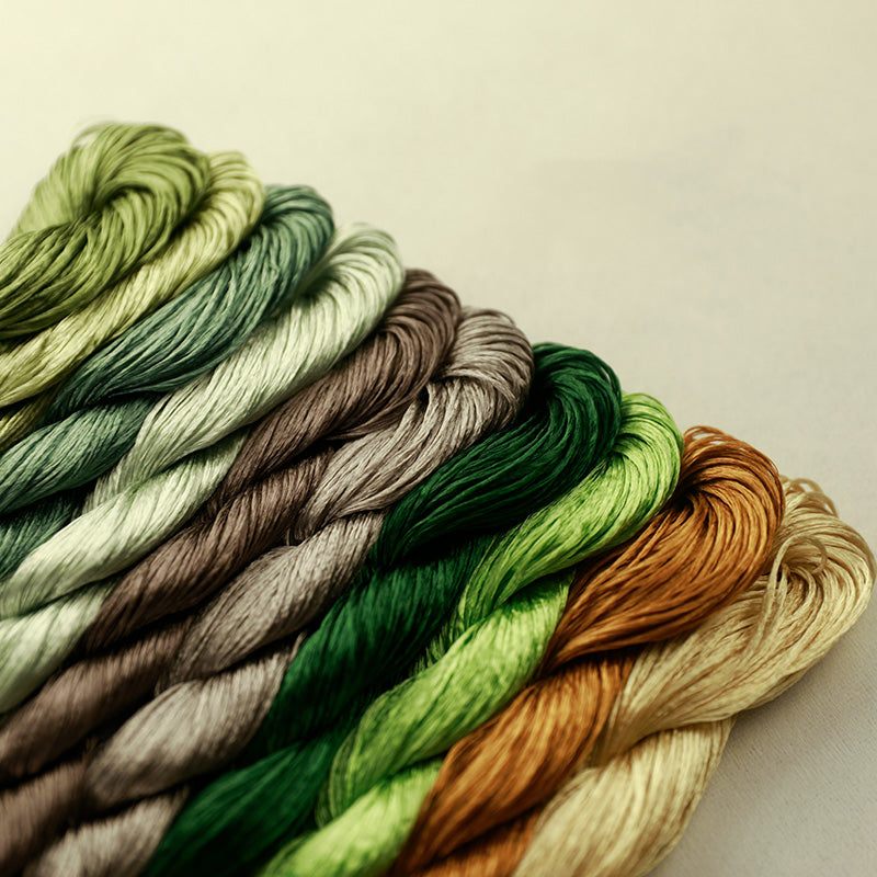Close-up of lustrous, no-split Suzhou embroidery thread in ten common leaf colors, featuring a rich palette of greens, browns, and golds for crafting