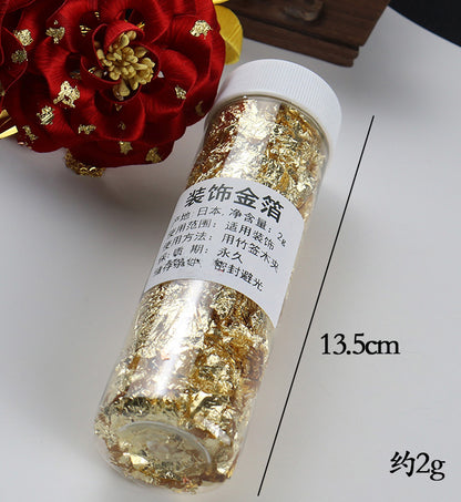 A 13.5cm jar filled with 2g of gold leaf flakes for DIY art projects and decoration.