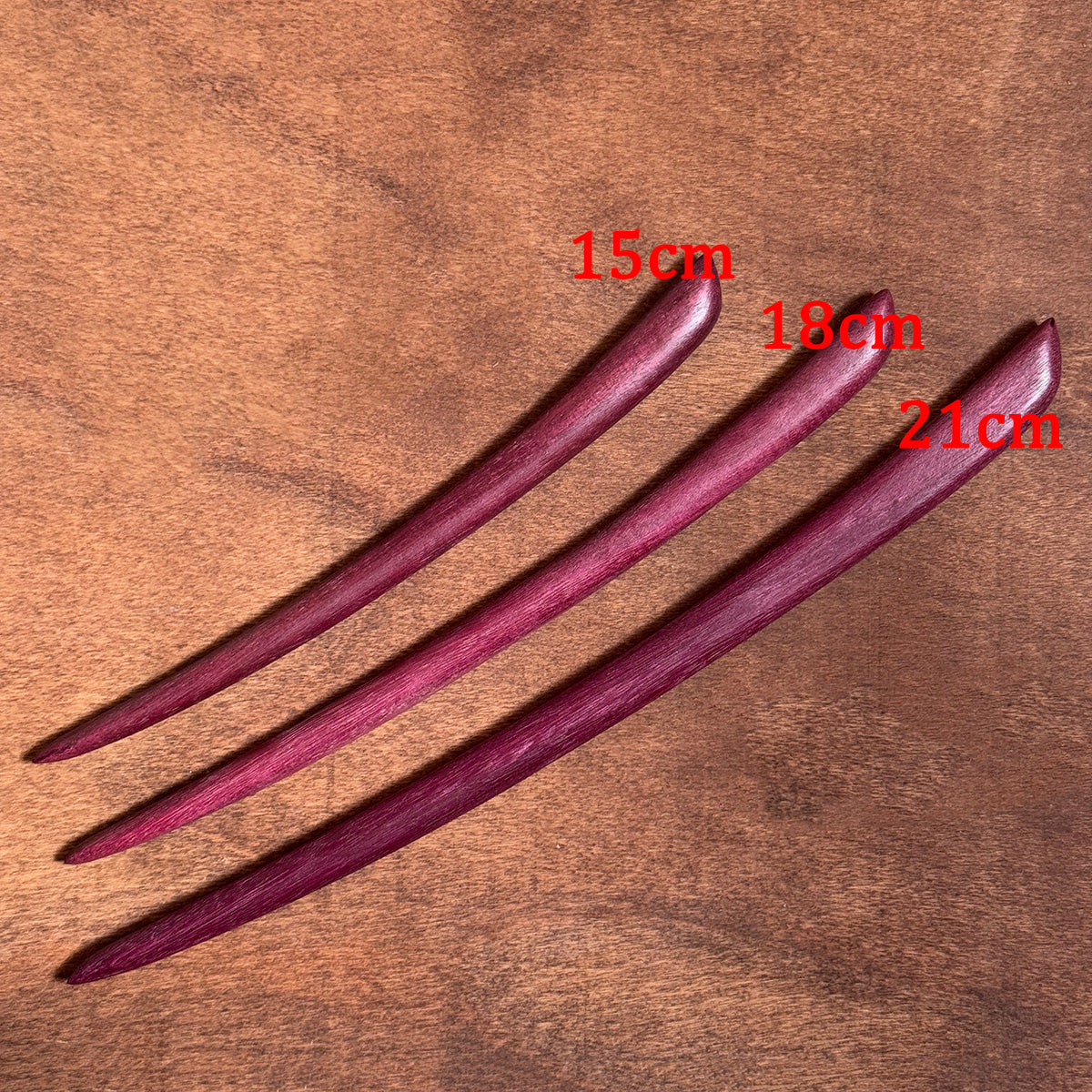 Three purpleheart wood hair sticks showing the different available lengths of 15cm, 18cm, and 21cm.