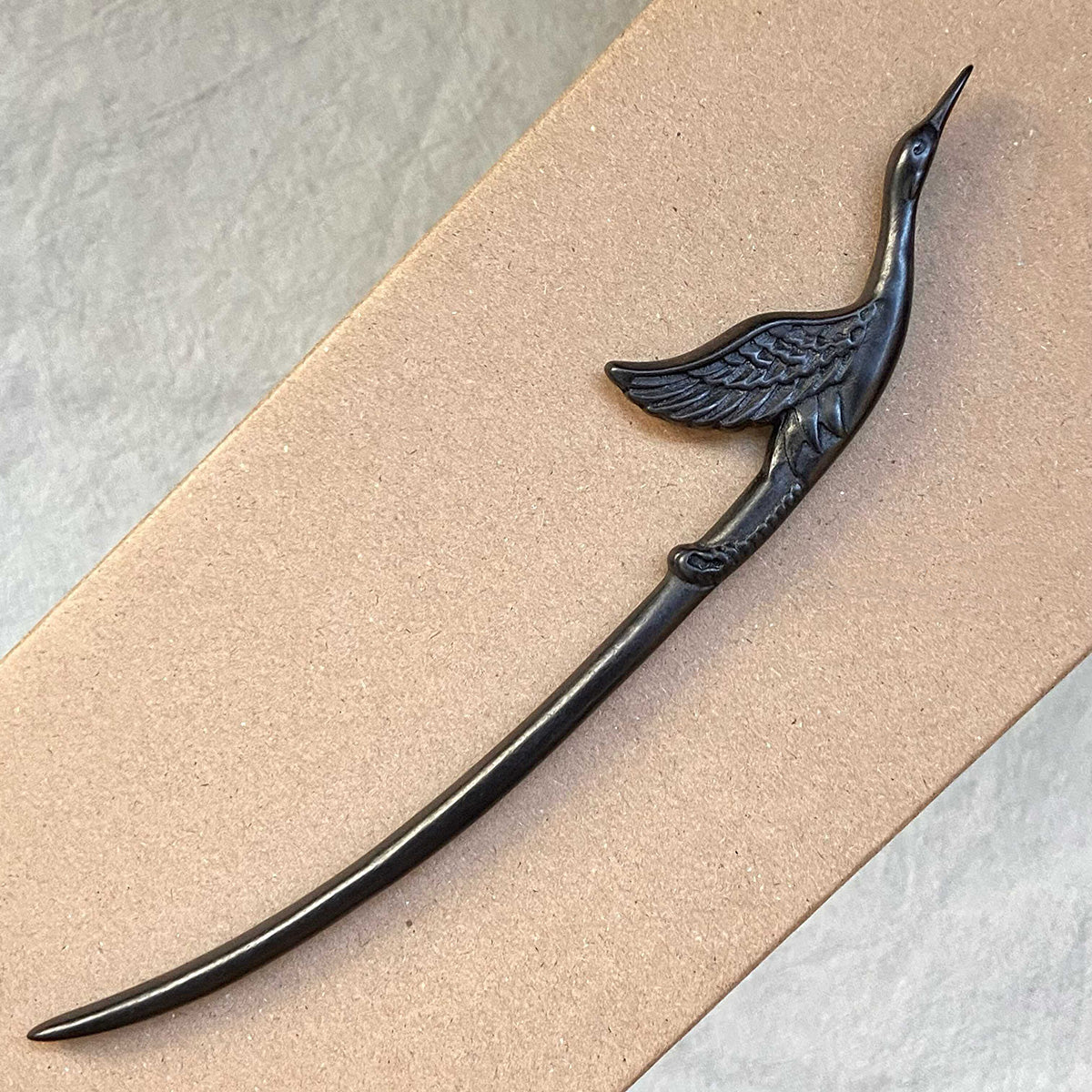 Hand-carved black ebony wood hair stick in a flying crane design shown on a neutral cardboard background.