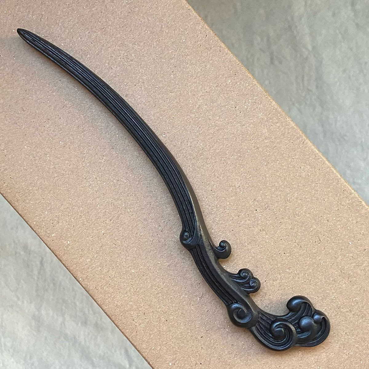 An overhead view of the intricately carved "Wave" wooden hair pin, showcasing its fluid design and the rich color of the African Blackwood.