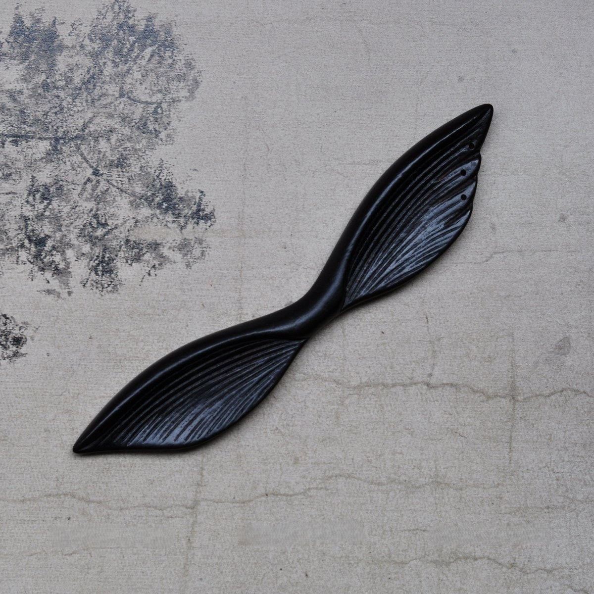 Top view of 13cm natural African Blackwood hair stick with Mysterious Wings design on textured fabric background.