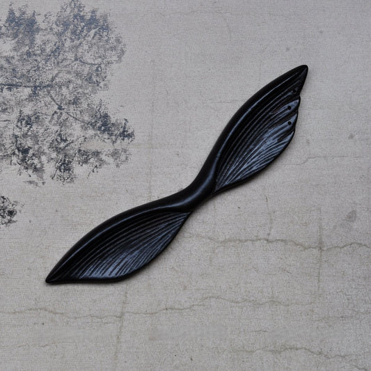 Top view of 13cm natural African Blackwood hair stick with Mysterious Wings design on textured fabric background.