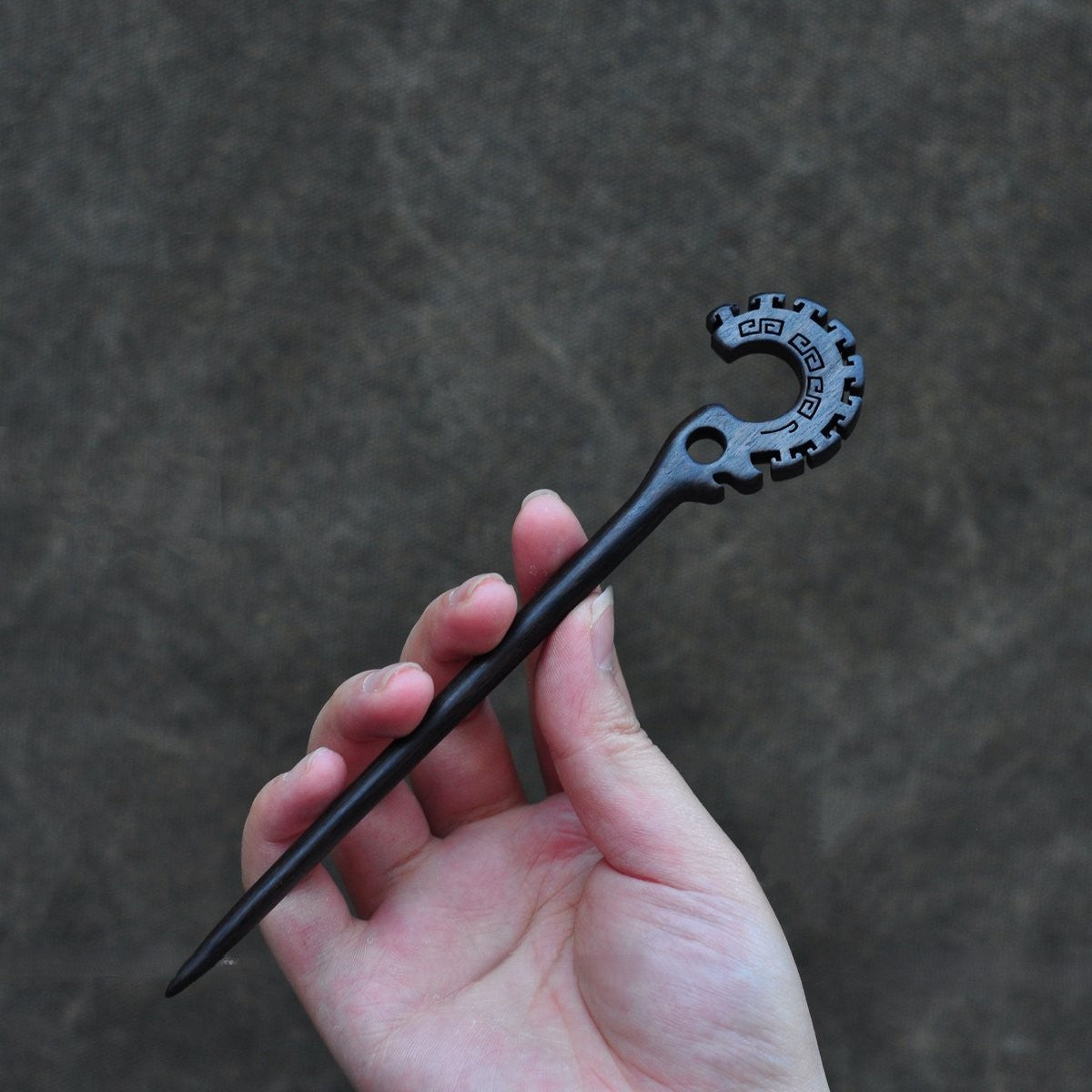 Natural African Blackwood hair stick "Jie Jie Shou" 18cm held in hand against textured background.