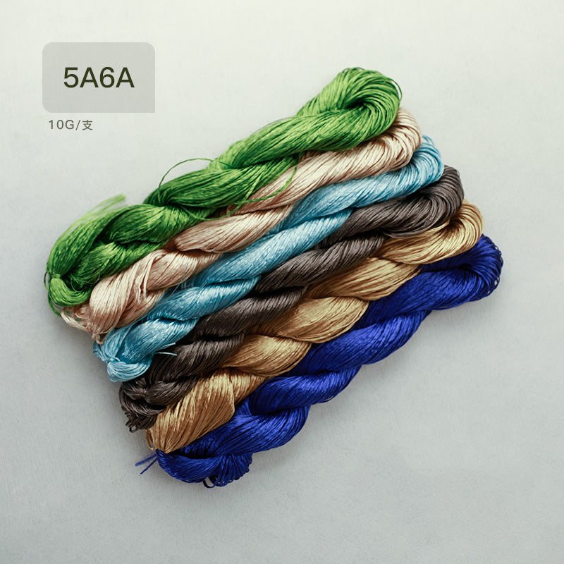 A flat-lay view of six 10g bundles of untwisted mulberry silk thread, labeled as the "5A6A" collection, showcasing a range of green, blue, brown, and gold colors.