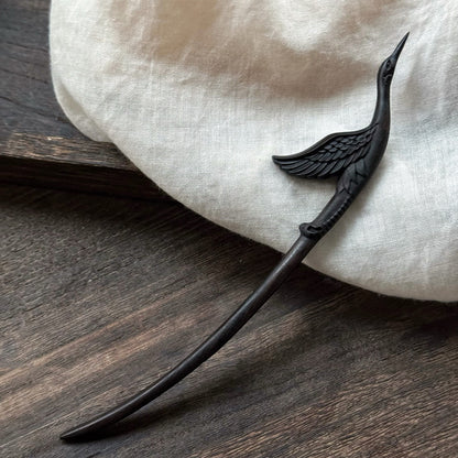 Elegant black ebony wood crane hairpin resting on a white linen cloth over a dark wood surface.