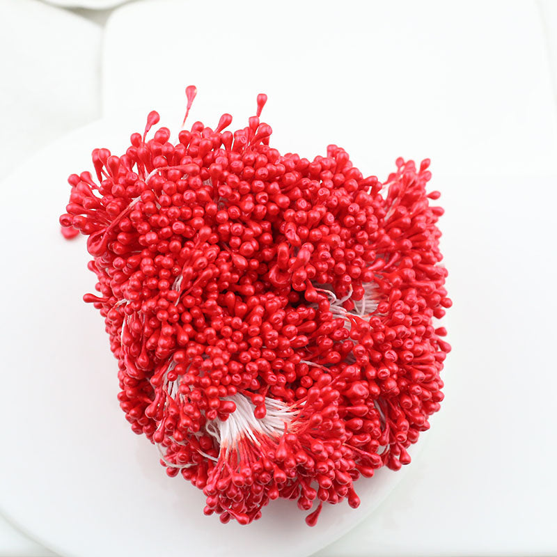 A close-up of a bundle of bright red 3mm glossy artificial flower stamens on a white surface, perfect for crafting vibrant silk and sugar flowers.