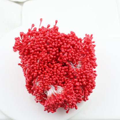 A close-up of a bundle of bright red 3mm glossy artificial flower stamens on a white surface, perfect for crafting vibrant silk and sugar flowers.