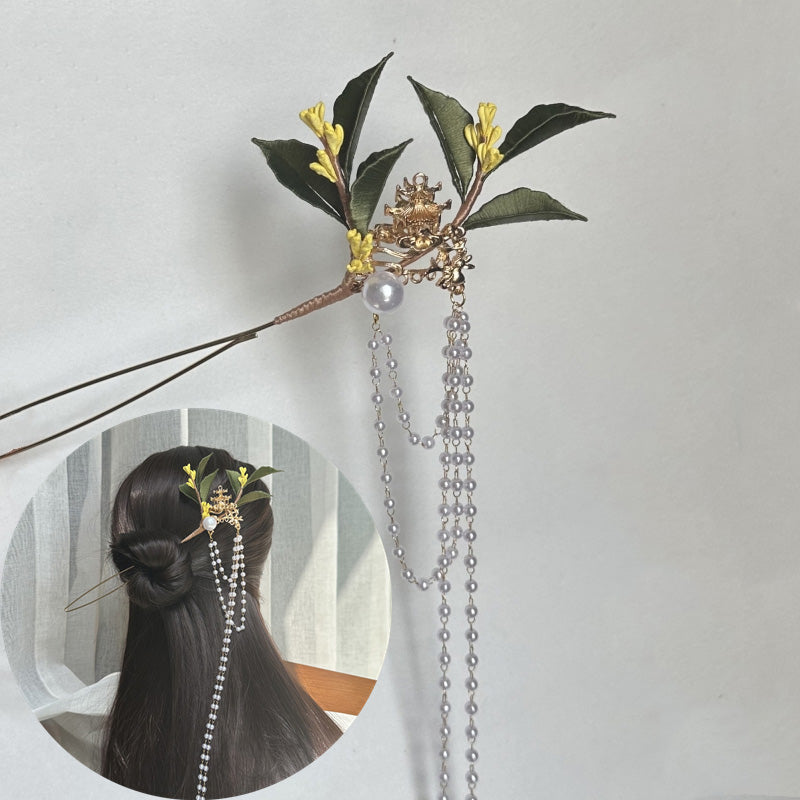 A finished handmade green and yellow fabric flower hairpin with long pearl chains, displayed as a hair accessory on a person with dark hair, highlighting the completed craft project.