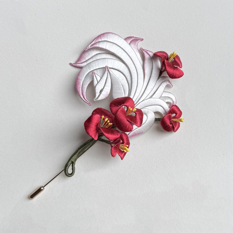 A finished handcrafted Chanhua brooch featuring a white and pink nine-tailed fox with vibrant red flowers.