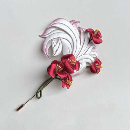 A finished handcrafted Chanhua brooch featuring a white and pink nine-tailed fox with vibrant red flowers.