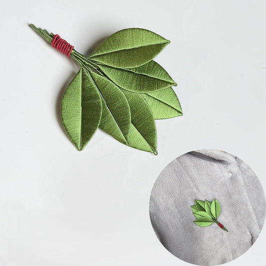 Finished DIY Chanhua pomelo leaf brooch made from silk thread, displayed on a soft grey coat.