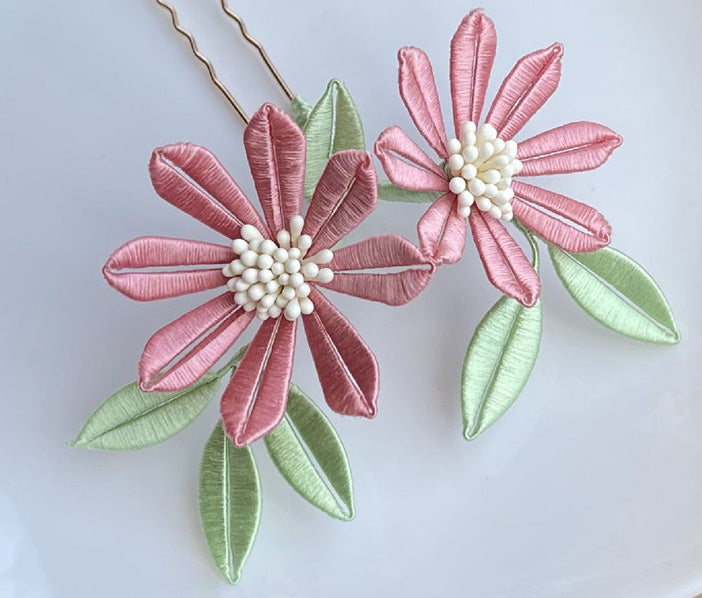 A finished handmade Sun Flower Chanhua hairpin with delicate pink petals and light green leaves, created from a DIY flower craft kit.