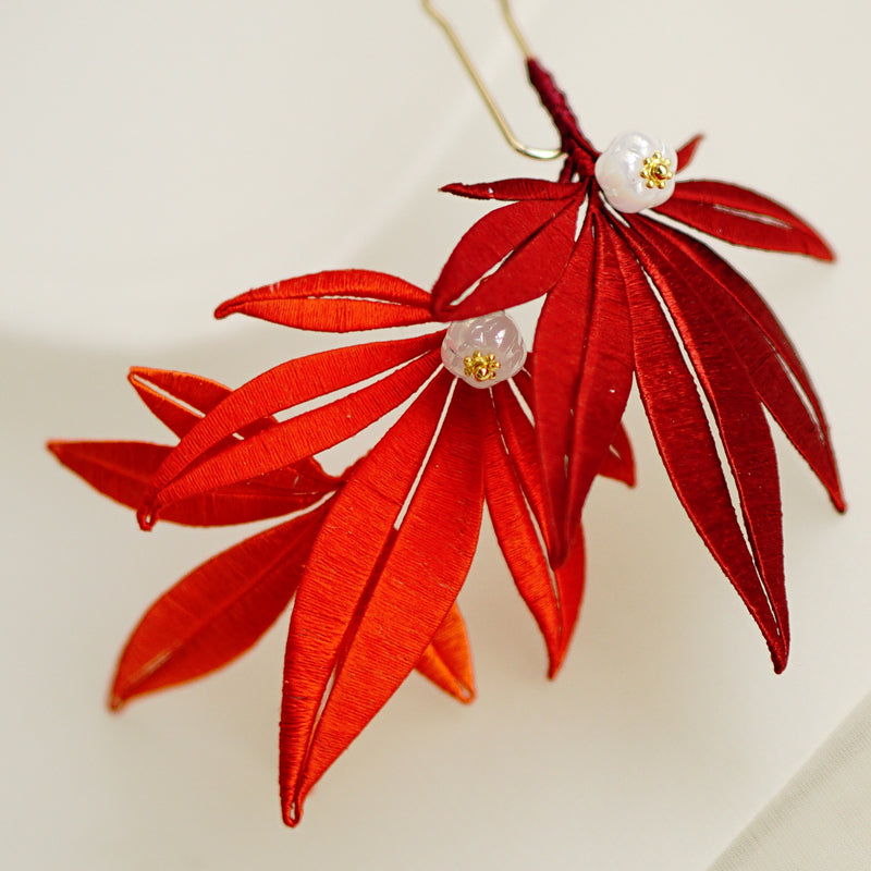 Close-up of a finished handmade red maple leaf hairpin with white and gold beads.
