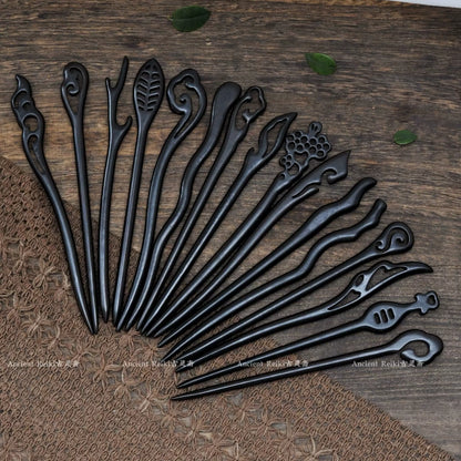 An artistic fan-shaped arrangement of various black sandalwood hairpins, showcasing a wide variety of carved tops, including floral and abstract shapes.