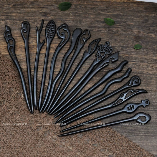 An artistic fan-shaped arrangement of various black sandalwood hairpins, showcasing a wide variety of carved tops, including floral and abstract shapes.
