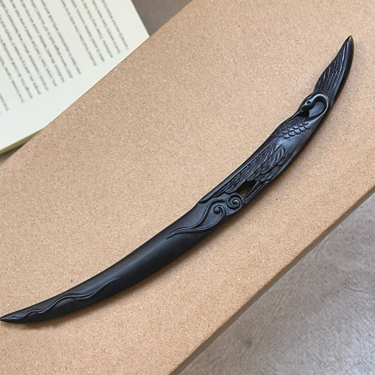 Natural African Blackwood hair stick with crane and moon design 18cm on wooden surface with book background.