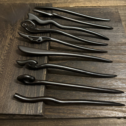 Set of 9 natural African Blackwood hair sticks, 21cm long curved designs, displayed on wooden surface.